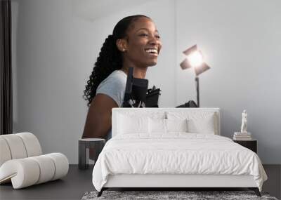 African American Female Videographer Posing with Video Camera in Hand on Film Set. Camera Woman is Proud and Smiling Looking Off Camera. Wall mural