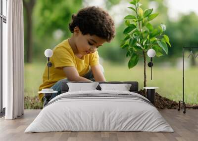 A young boy planting a small tree in the ground, symbolizing hope, growth, and environmental care in a lush green setting. Wall mural