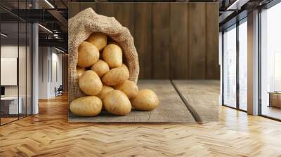 Fresh potatoes spilling from a burlap sack, set against a rustic wooden background, ideal for culinary themes. Wall mural