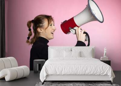 Funny young female shouting through megaphone. Young woman using loudspeaker on colored backgrounds Wall mural