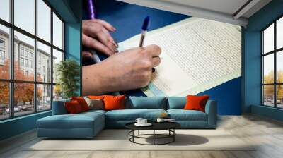 a person is writing with a blue pen on paper in the middle of their hand Wall mural