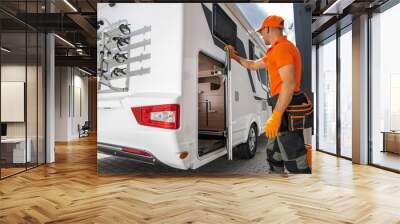 A technician in orange uniform inspecting the rear compartment of a white RV Wall mural