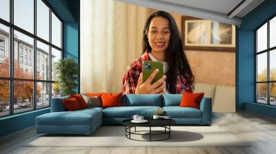 a young woman is standing in the living room looking at her phone Wall mural