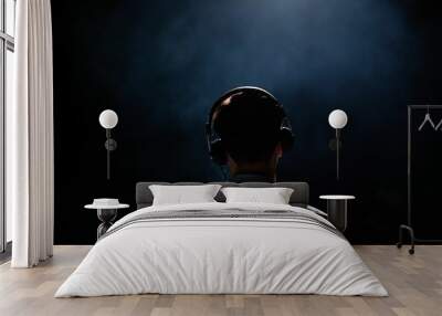 Back view of a man wearing headphones in a dark room with a spotlight illuminating him Wall mural