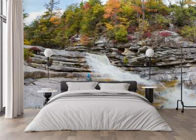 Child enjoying a peaceful moment at a majestic waterfall surrounded by natural rock formations Wall mural