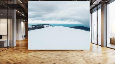 Scenic mountain range landscape covered with snow in winter under a dark, cloudy sky Wall mural