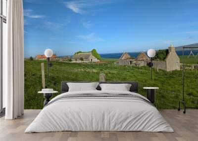 Scenic view of old stone buildings and green fields with ocean in background. Wall mural