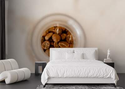 Small glass jar filled with roasted coffee beans on a white table Wall mural