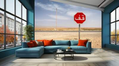 Stop sign with Arabic text in a desert landscape under a clear blue sky Wall mural