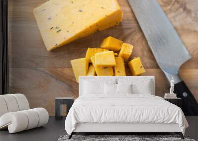 Top view of a knife resting on a wooden cutting board with chunks of English cheddar cheese Wall mural