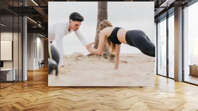 Young athletic couple exercising at the beach in a planking pose Wall mural