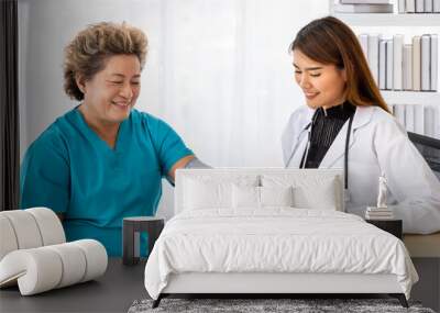 Asian female medical doctor measuring blood pressure senior elderly patient, looking at camera Wall mural