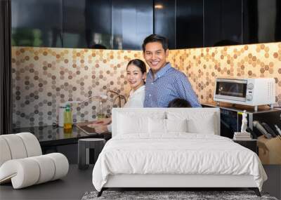 Beautiful young Asian woman mother with man husband and young boy son family washing dishes in modern kitchen room, looking at camera Wall mural