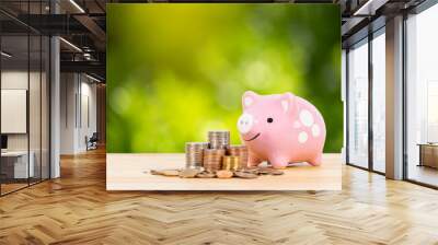 Pink piggy bank with coin stack steps with sunlight ray on green tree background, with hand inserting money Wall mural