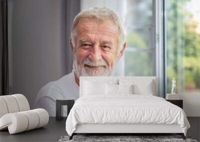 Senior elderly man standing at window in bedroom after waking up in morning, looking camera Wall mural