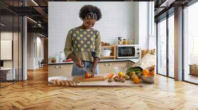 Young beautiful African black girl woman cutting tomato in kitchen for cooking, food and meal preparation. Wall mural