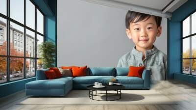 A cheerful young boy with a charming smile, wearing a traditional outfit against a soft gray background. Wall mural