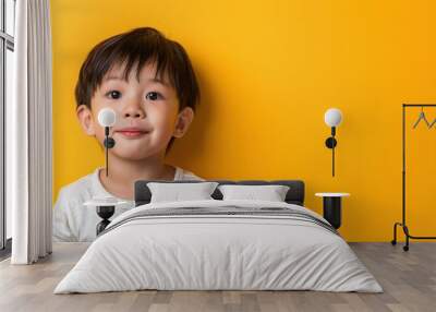 A happy young boy with short black hair smiling against a bright yellow background, embodying joy and innocence. Wall mural