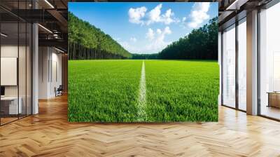 A vibrant green field with a clear blue sky and fluffy white clouds, lined by tall trees on one side, perfect for outdoor activities. Wall mural