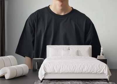 A young man poses confidently in a stylish oversized black t-shirt, showcasing modern fashion trends and casual styles. Wall mural