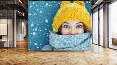 Cheerful person in a cozy yellow hat and scarf, enjoying a snowy winter day with bright blue eyes and a warm smile. Wall mural