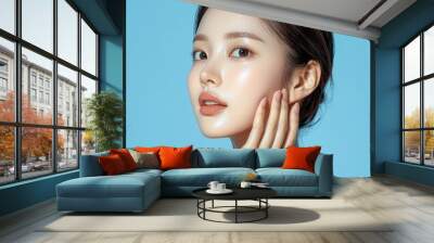 Portrait of a young woman touching her face against a blue background, radiating beauty and confidence. Wall mural