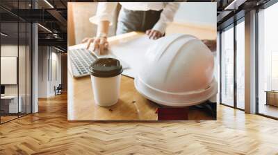 Young Architect Team meeting present time, Engineer working with new startup construction project in office room with hot coffee cup and safety helmet in office, Construction Concept. Wall mural