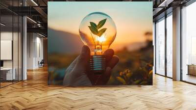 A hand holding a light bulb with a plant inside, set against a clear sky, symbolizing innovative solutions for decreasing carbon emissions and environmental care Wall mural