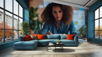 A young woman with curly hair sits at a desk in an office, focused on writing on a piece of paper. Wall mural