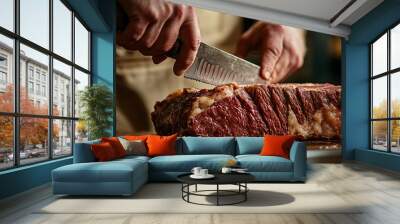 Close-up of a chef's hand slicing a large cut of beef with a serrated knife. Wall mural