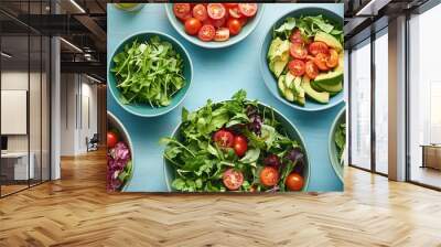 Different types of green salad with cherry tomatoes and avocado slices in bowls on a blue wooden table. Wall mural