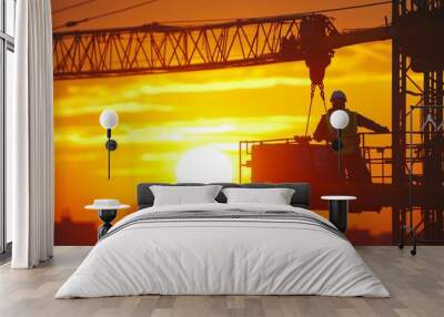 Silhouette of a construction worker operating a crane against a vibrant sunset. Wall mural