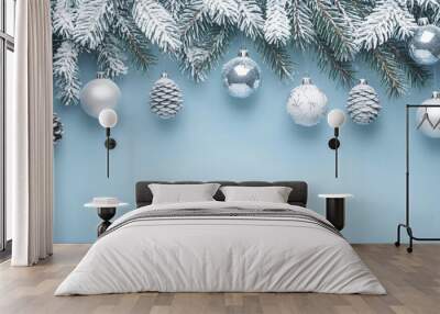 Snowy pine branches with silver ornaments and pine cones on a light blue background. Wall mural