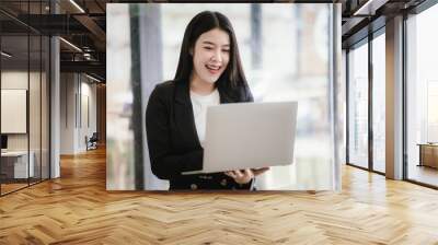 Beautiful Asian businesswoman talking on the phone using laptop in office Wall mural