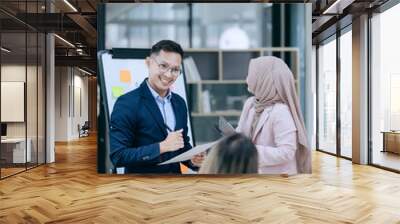 In a corporate meeting, a businessman leads a discussion on financial strategy, pointing at charts and graphs. The team collaborates on planning and analysis, using laptops and paperwork to ensure suc Wall mural