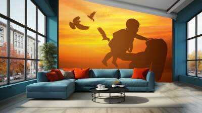 Silhouette of mother and child playing at sunset with flying birds. Wall mural