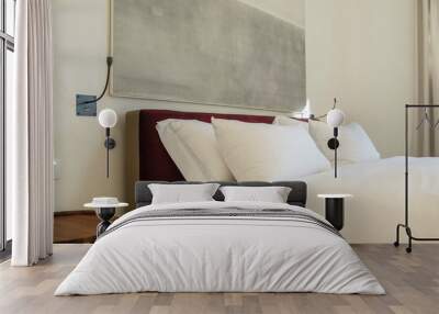 Details of the bedroom interior in light colors close-up - a fragment of a bed with two large white pillows, a lamp with a night light and a bedside table Wall mural