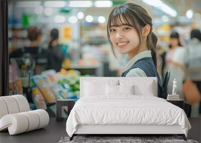 A young adult Japanese female cashier stands proudly at her checkout station, smiling as she rings up items. The background is filled with colorful products and cheerful shoppers, enhancing the Wall mural