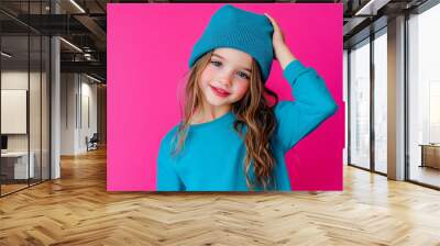 Charming girl, wearing fashionable blue clothes, touching her head gently, smiling cutely against a vibrant pink backdrop. Wall mural