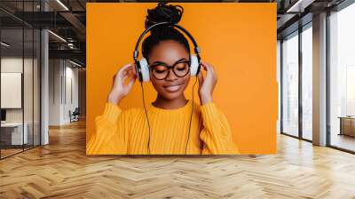 Young African American woman wearing headphones on a orange background listening to her favorite music Wall mural