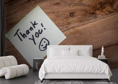 A thank you note is written on a piece of paper and placed on a wooden surface. The note is accompanied by a smiley face, which adds a positive and friendly tone to the message Wall mural