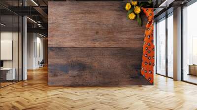 A decorative orange tie with Halloween motifs, accompanied by a pumpkin and yellow flowers, is displayed on a rustic wooden surface. Wall mural