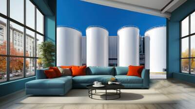 A series of white cylindrical silos against a bright blue sky, showcasing a modern industrial facility. Wall mural