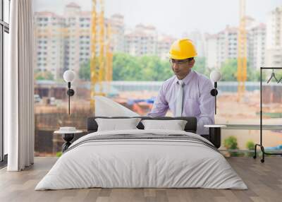 indian male architect reading plans with construction background Wall mural