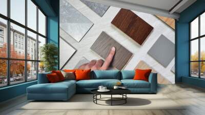 interior designer's hand choosing material samples including wooden engineering flooring tiles, grainy quartz stones, concrete tiles, wooden vinyl flooring tile, marble artificial stone. mood board. Wall mural