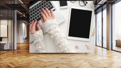 Top view of woman's hands typing on laptop keypad placed on white office desktop with blank smartphone, decorative plant and supplies. Mock up. Technology devices view from above. Office equipment. Wall mural