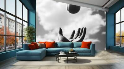 A hand is gracefully throwing tennis ball into air against backdrop of fluffy clouds, capturing moment of motion and freedom Wall mural