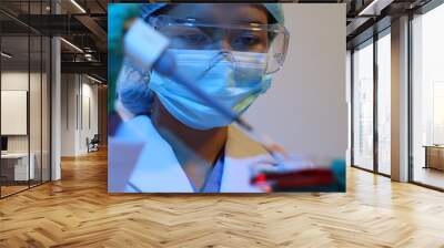 Scientists are doing research in a science lab. A medical chemist in a white coat, gloves and goggles looks at a glass tube. Compare two different liquid samples. and discuss future experiments. Wall mural