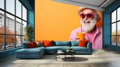 Vibrant and colorful summer concept with a happy old man in a hat and sunglasses sipping an orange juice or cocktail on a pastel background A trendy hipster senior person enjoying Wall mural