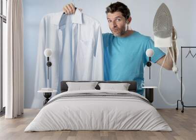 young attractive and satisfied man holding iron and slick shirt smiling happy and cocky Wall mural